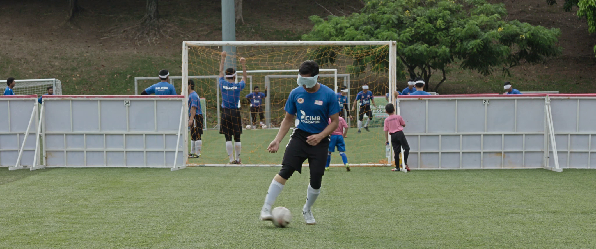 Blind footballer Asri is dribbling a ball alone while his teammates train in the background.