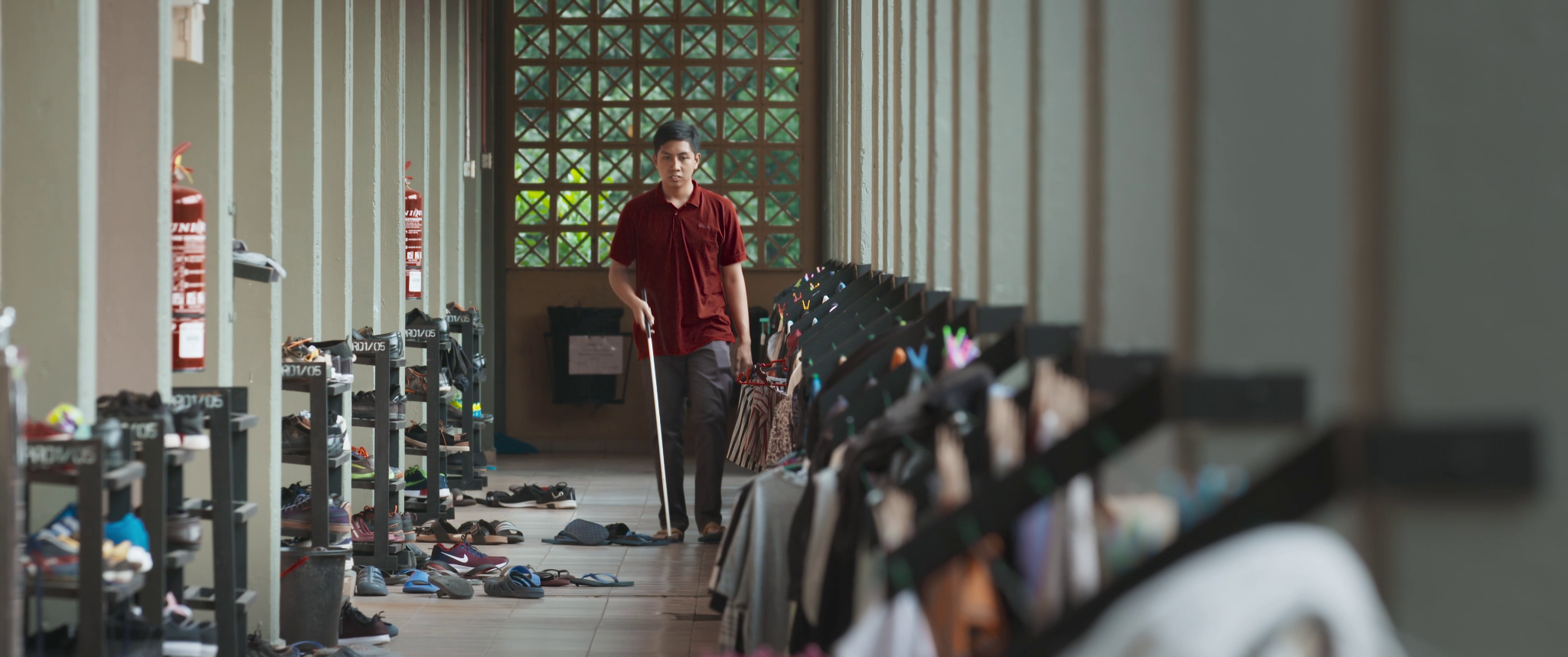 Blind footballer Asri walks down a corridor at his university hostel with his white cane.