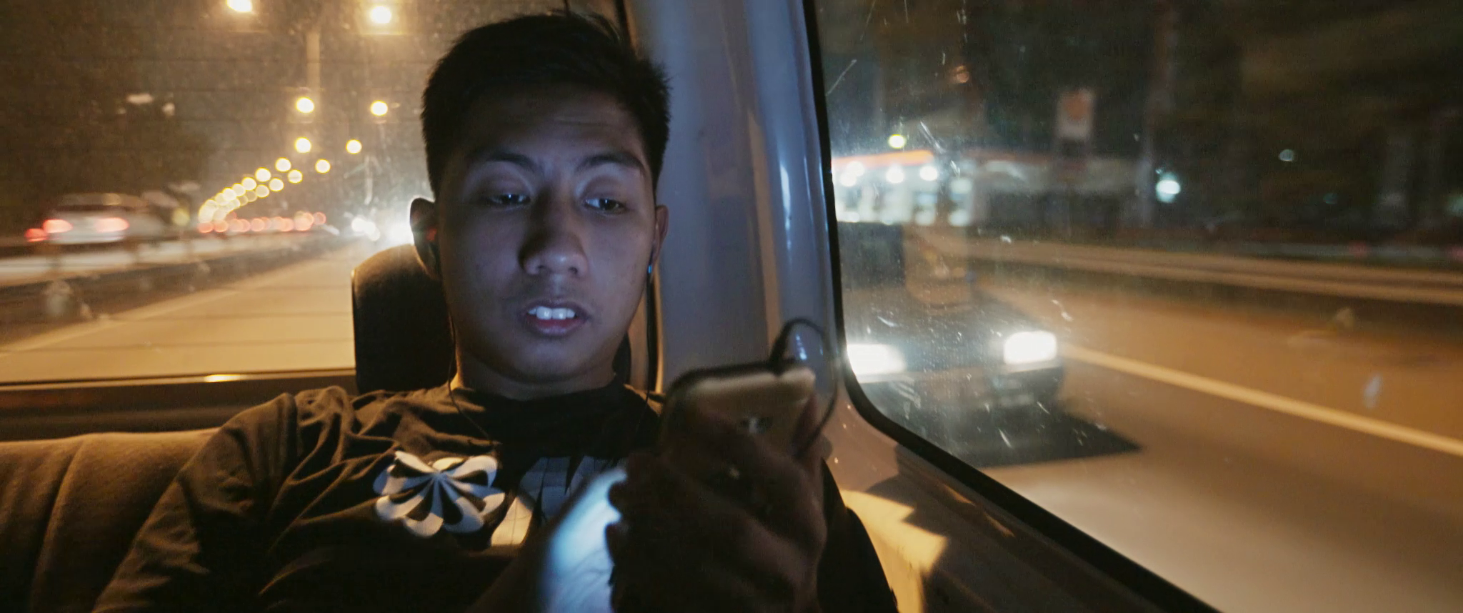 Blind footballer Asri is traveling in a van at night, drawn to his mobile phone.