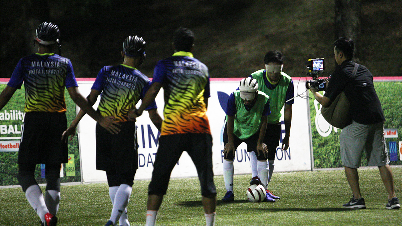 Juru sinematografri Chin Hor merakam dua orang pemain bola sepak bersedia untuk memulakan permainan di atas padang.